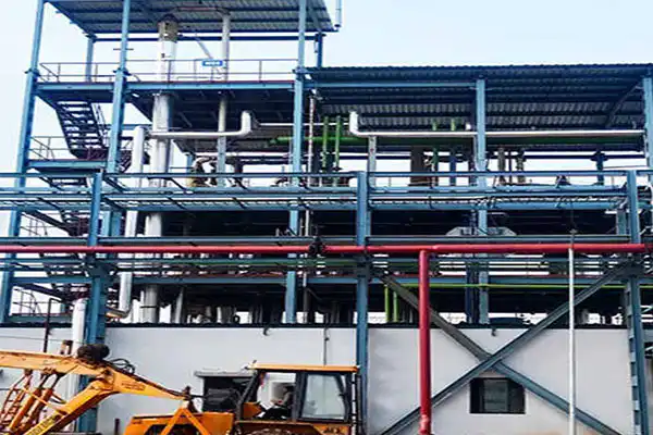 Industrial facility with a multi-level steel framework, platforms, and network of pipes; construction equipment visible in the foreground.